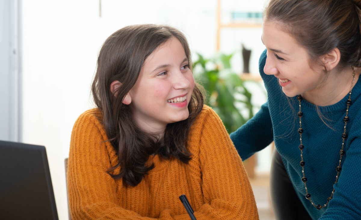 young woman helps a teen girl with homework Positive disability support interaction