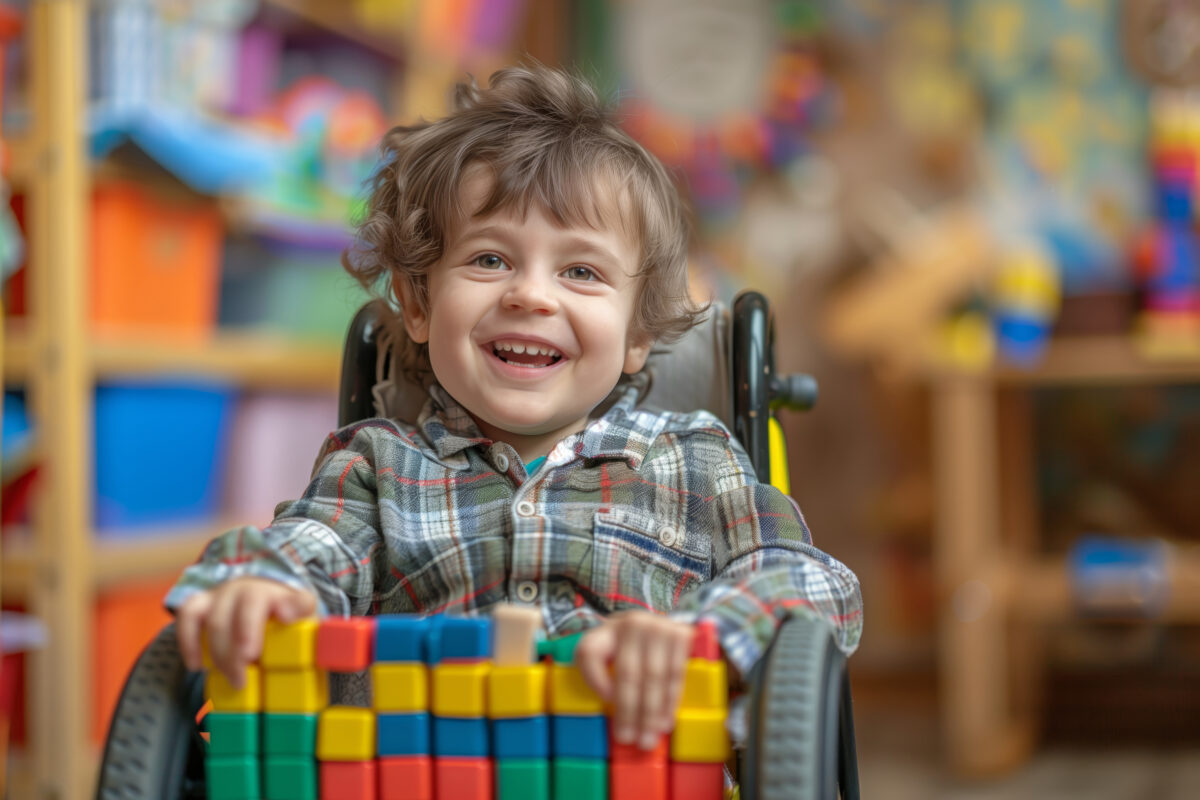 Smiling boy in a wheelchair plays with blocks in a classroom Happy child early intervention supports