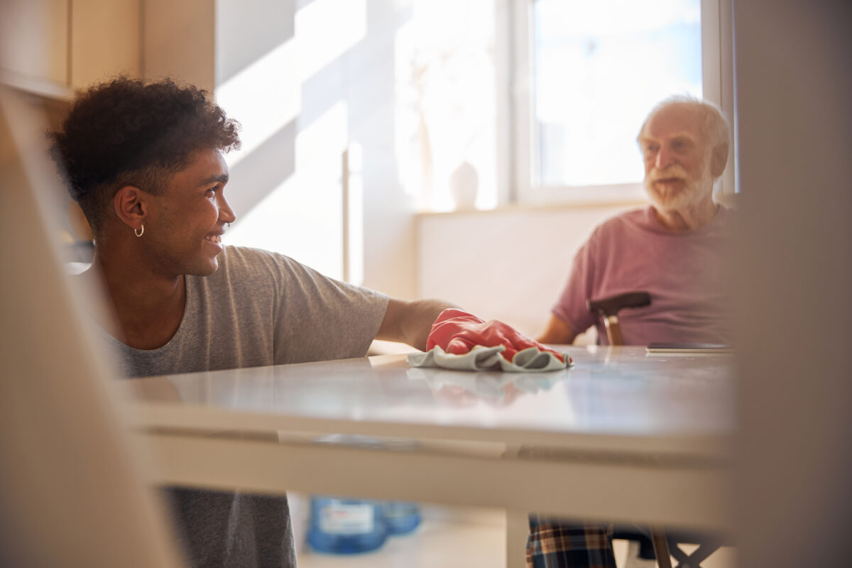 Dark-haired volunteer cleaning the disabled man kitchen applying for aged care funding support
